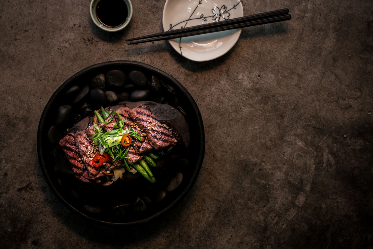 Sliced steak in a black bowl on rough concrete table