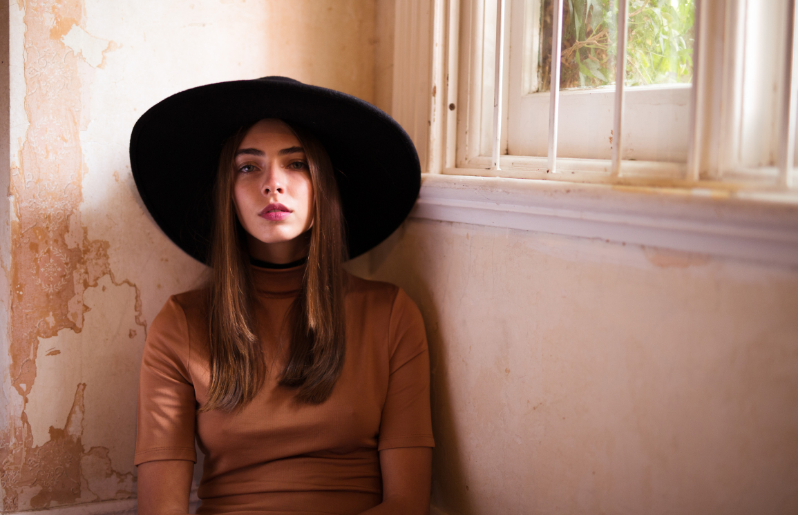 Portrait of a woman in wide brim black hat against a weathered wall