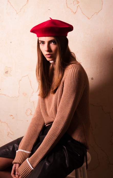 Woman in red beret and camel knit sweater against textured wall